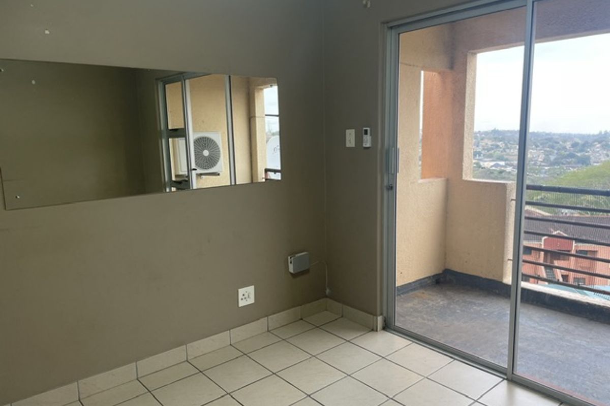 An empty living area featuring tiled flooring and a large sliding glass door providing access to a balcony with an outdoor view.