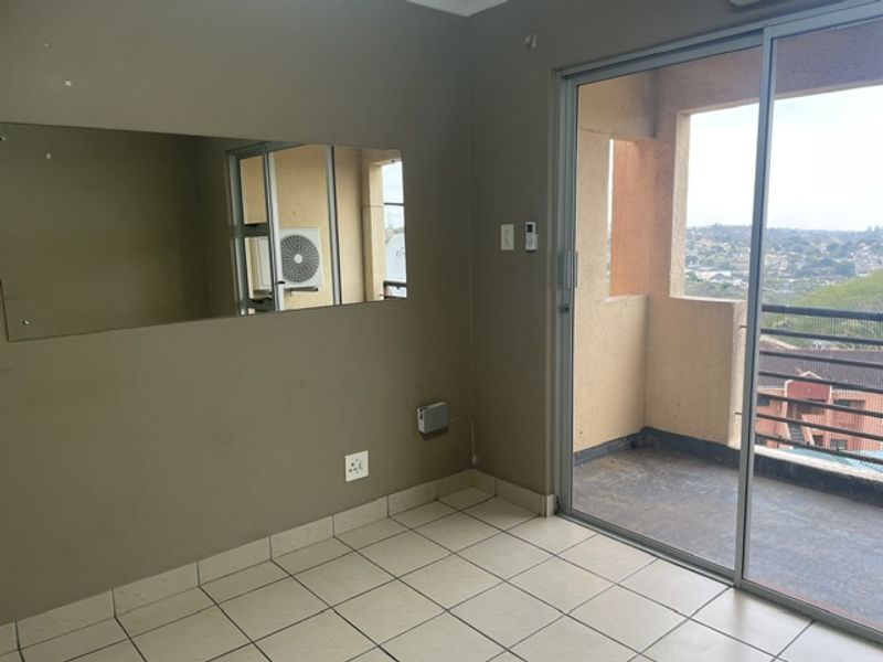 An empty living area featuring tiled flooring and a large sliding glass door providing access to a balcony with an outdoor view.