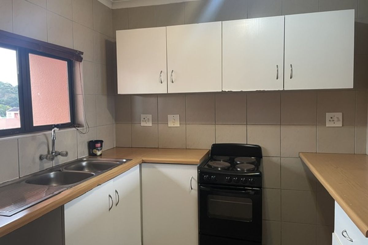 Functional kitchen featuring laminate countertops, double bowl stainless steel sink, tiled splashback, and white cabinetry with a freestanding electric stove.