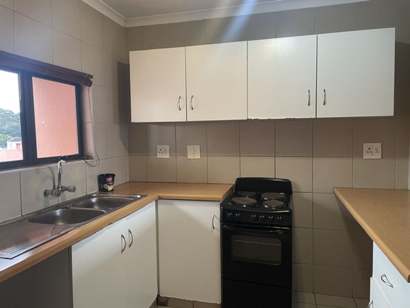Functional kitchen featuring laminate countertops, double bowl stainless steel sink, tiled splashback, and white cabinetry with a freestanding electric stove.