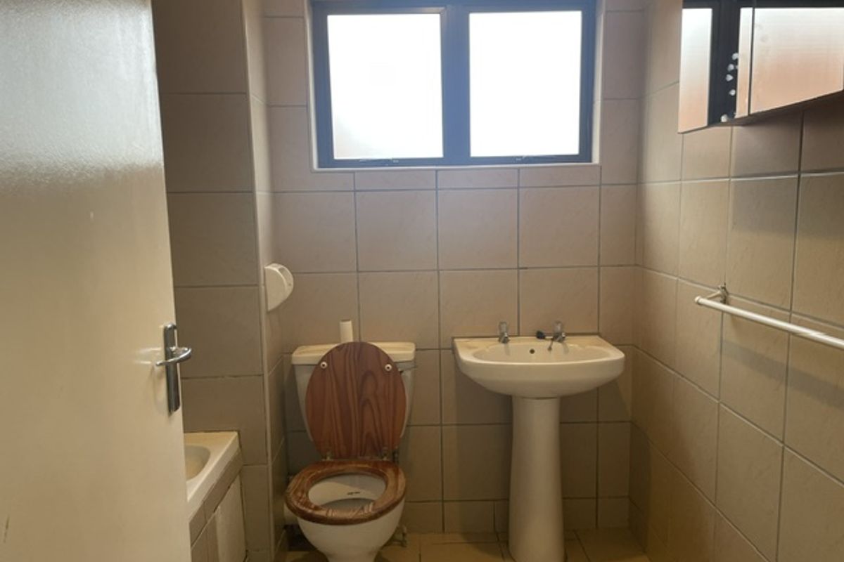 A functional bathroom featuring a pedestal basin, toilet, and fully tiled walls with a window for natural light.