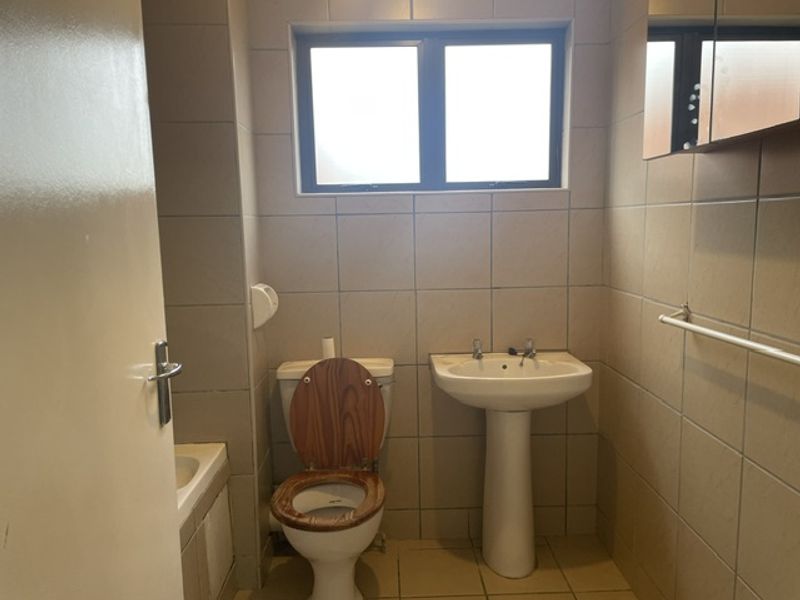 A functional bathroom featuring a pedestal basin, toilet, and fully tiled walls with a window for natural light.
