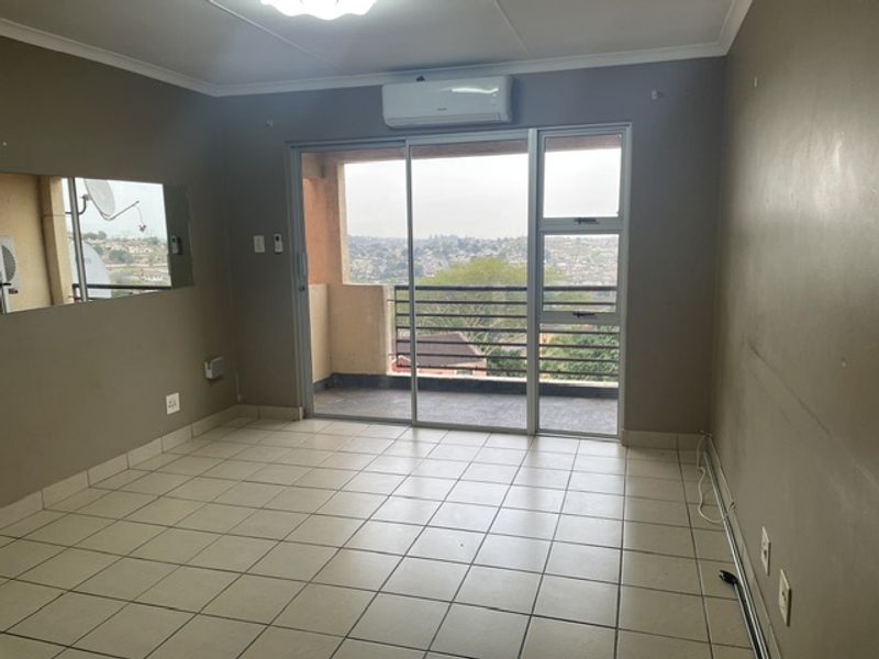 An empty living room featuring tiled flooring, a wall-mounted air conditioner, and sliding glass doors leading to a balcony with an elevated view.