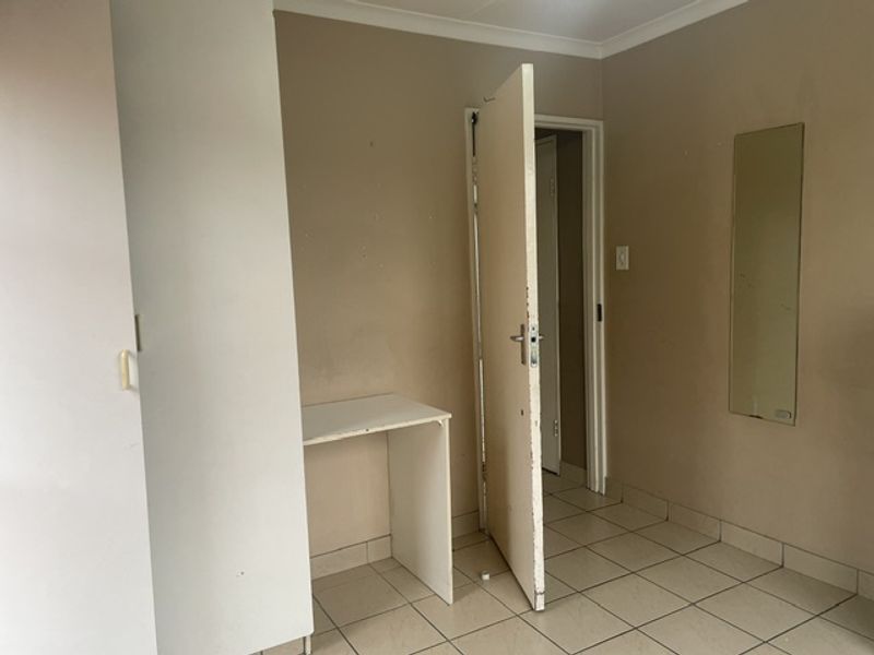 An empty bedroom featuring tiled flooring, a built-in wardrobe, and neutral wall tones, offering a blank canvas for personalization.