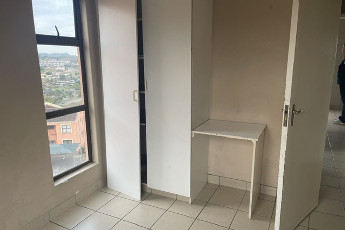 A compact bedroom featuring tiled flooring, a built-in wardrobe, and an integrated desk, offering a functional space with a view.