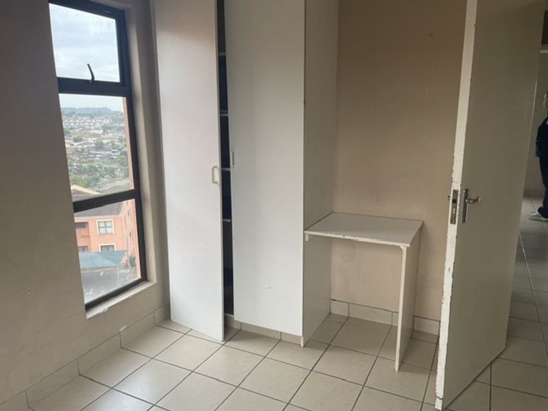 A compact bedroom featuring tiled flooring, a built-in wardrobe, and an integrated desk, offering a functional space with a view.