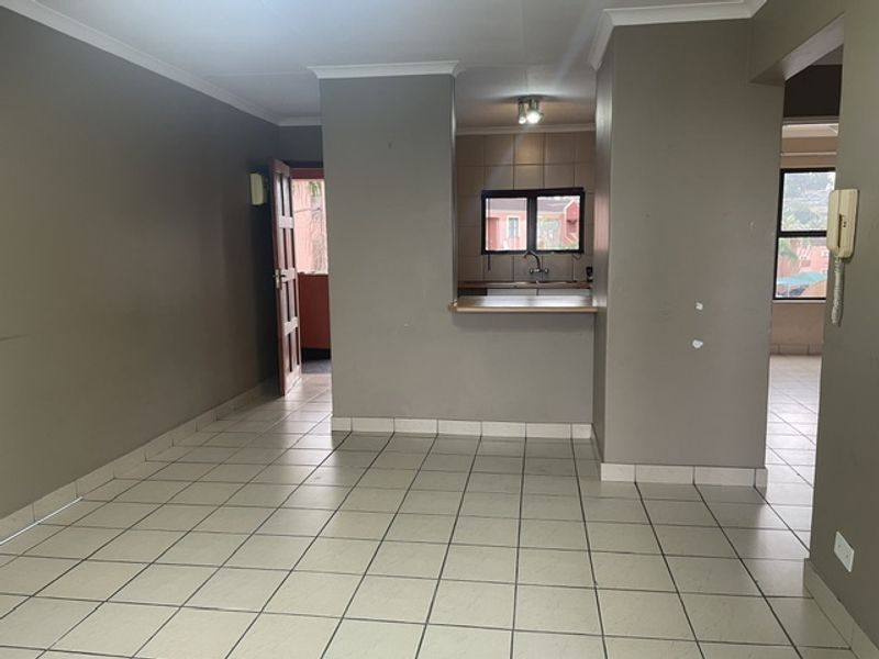 An open-plan living and kitchen area featuring tiled flooring, a breakfast bar, and neutral wall tones, presenting a blank canvas for potential interior design.