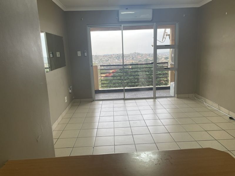 An empty living room featuring tiled flooring, an air conditioning unit, and sliding glass doors leading to a balcony with elevated views.