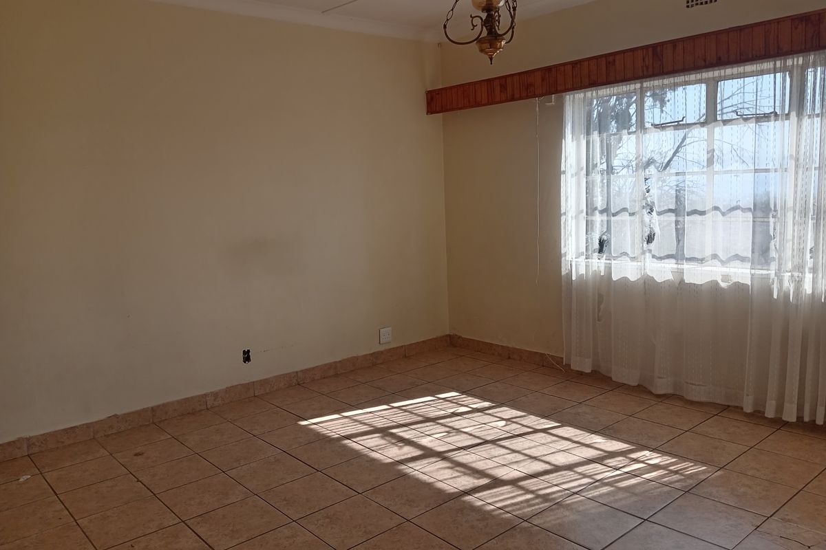 An empty living room featuring ceramic floor tiles, a timber curtain pelmet, and natural light through a large window.
