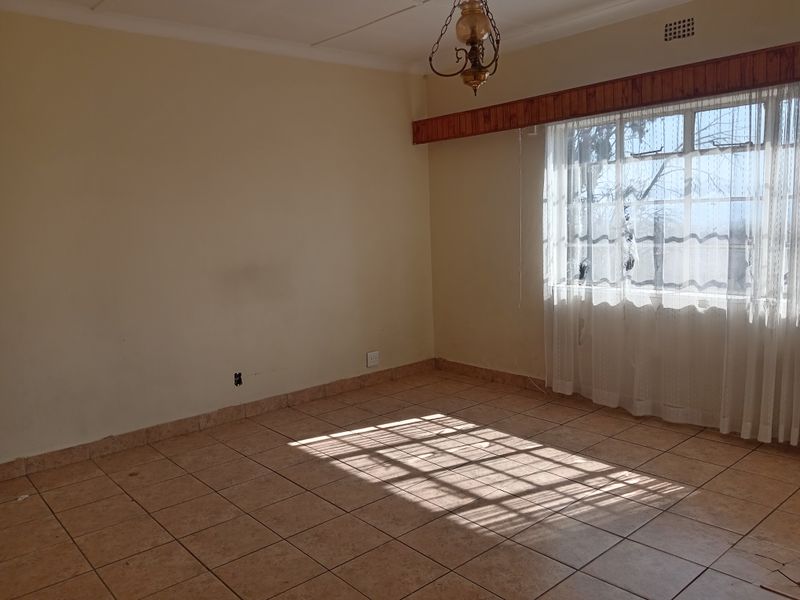 An empty living room featuring ceramic floor tiles, a timber curtain pelmet, and natural light through a large window.