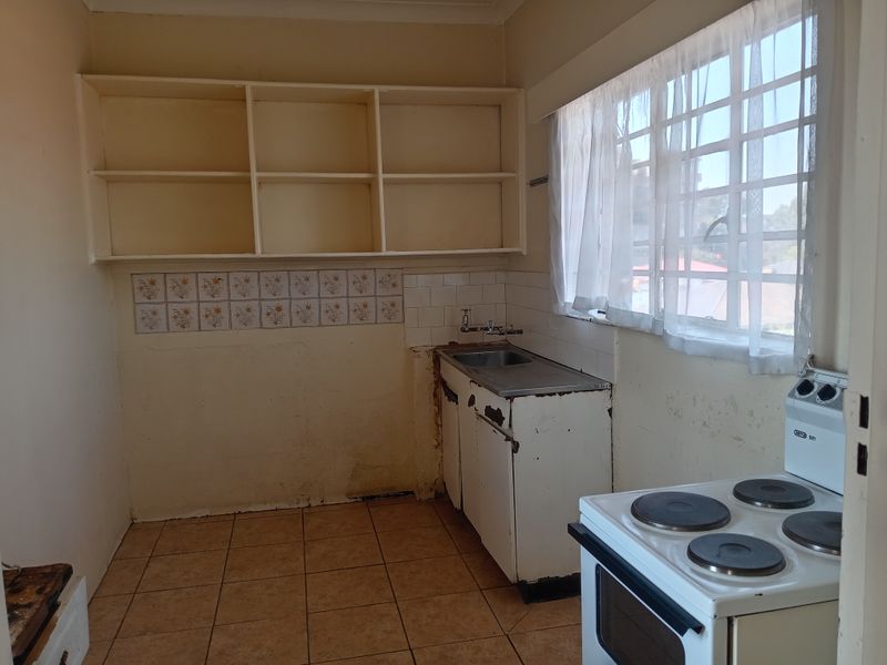 A dated kitchen featuring basic cabinetry, a stainless steel sink, open shelving, and tiled flooring, requiring renovation to modernize the space.