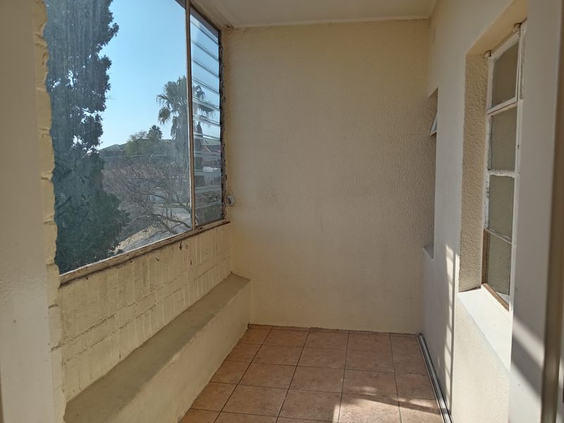A covered balcony area featuring tiled flooring, a built-in masonry bench, and large louvre windows overlooking the surrounding area.