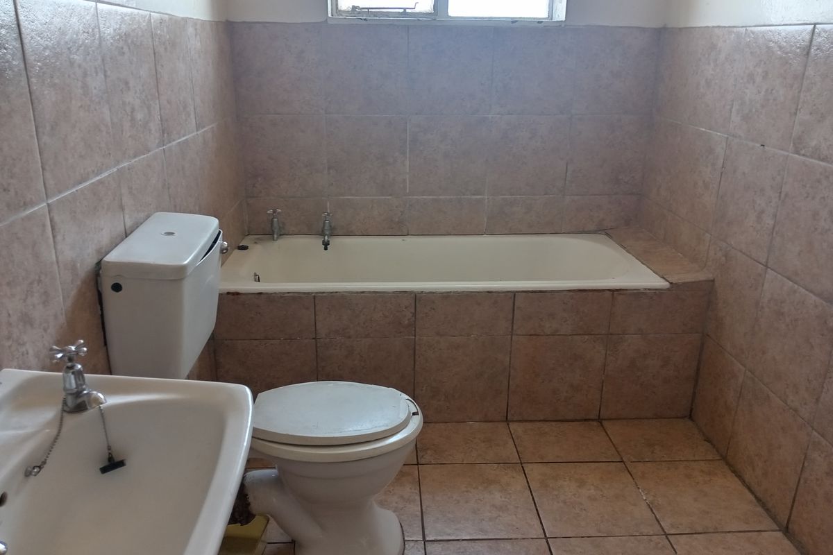 A dated bathroom featuring a built-in bathtub, pedestal basin, and toilet with full-height ceramic wall tiling.