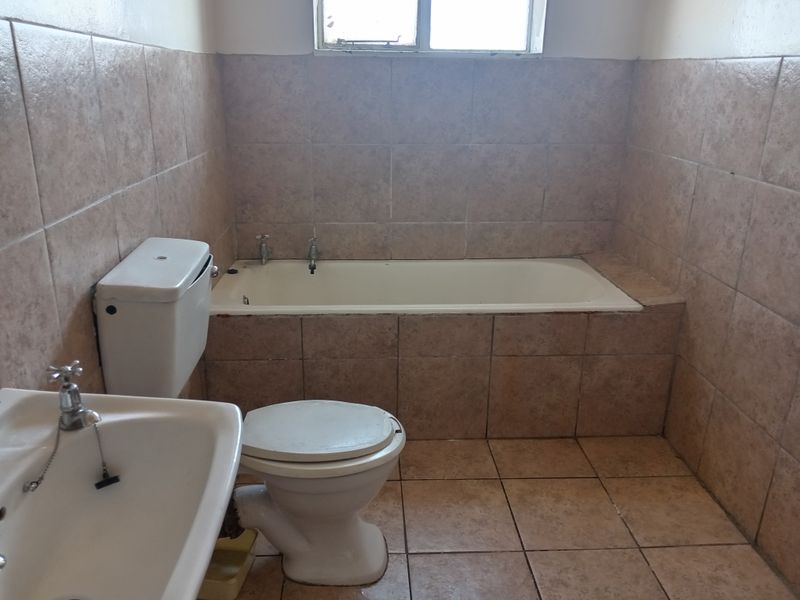 A dated bathroom featuring a built-in bathtub, pedestal basin, and toilet with full-height ceramic wall tiling.