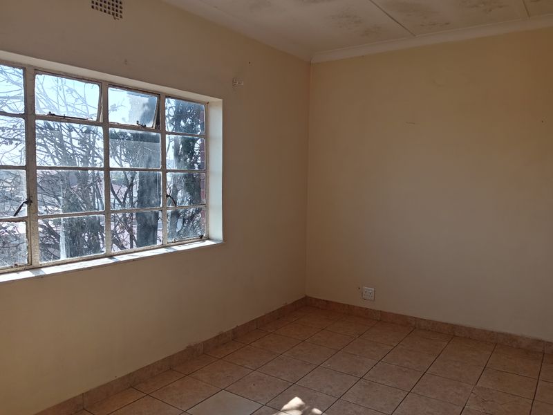 An empty bedroom featuring tiled flooring and a large steel-framed window, requiring cosmetic updates and ceiling repairs.