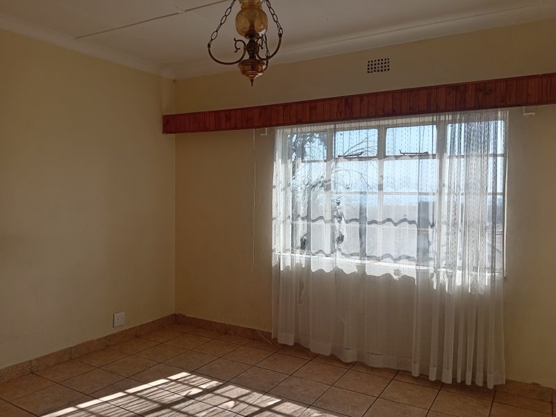 An empty living room featuring tiled flooring, a timber window pelmet, and a large metal-framed window providing natural light.