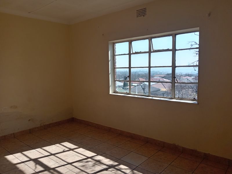 An empty bedroom featuring tiled flooring and a large steel-framed window with views of the surrounding neighborhood.