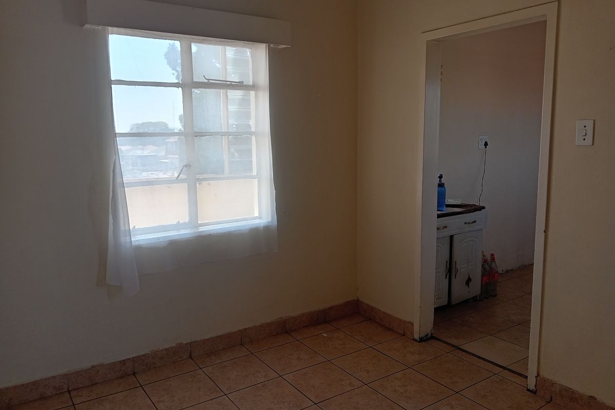 An empty bedroom featuring tiled flooring and a steel-framed window, with a doorway leading to an adjacent room.