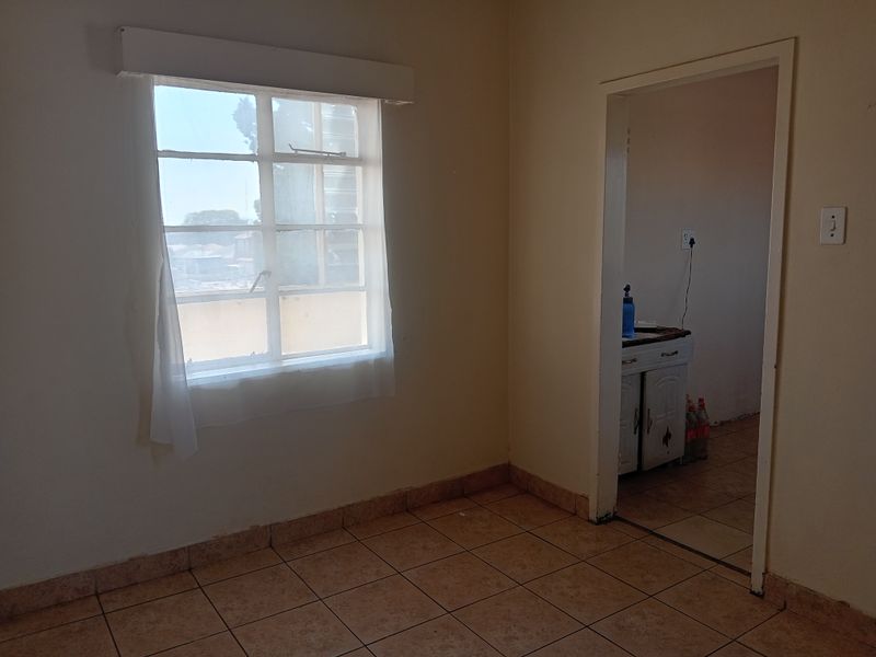 An empty bedroom featuring tiled flooring and a steel-framed window, with a doorway leading to an adjacent room.