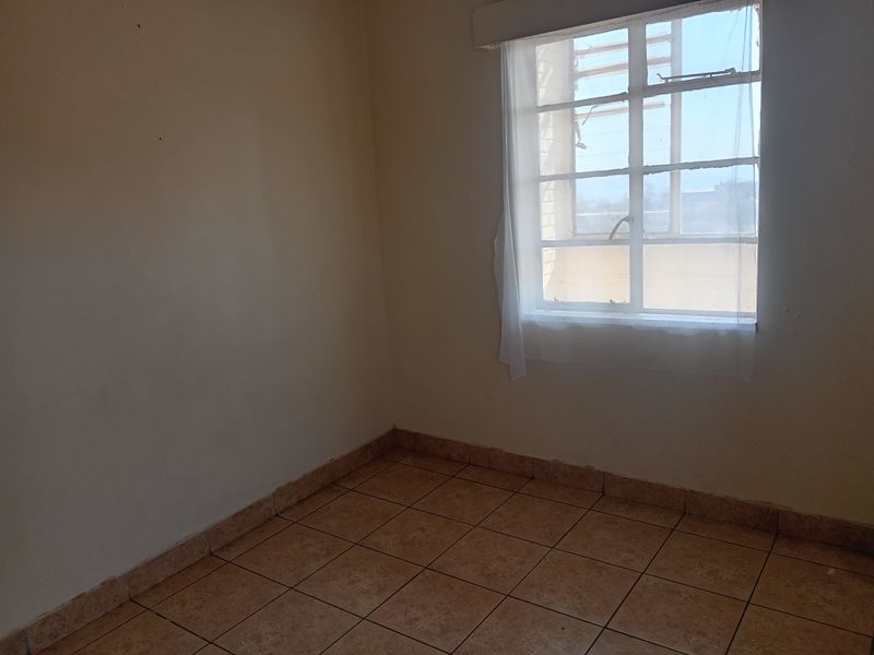 An empty bedroom featuring tiled flooring and a window with security bars, offering a blank canvas for potential renovation or staging.