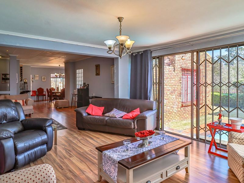 Spacious open-plan living area featuring laminate flooring, large sliding glass doors with security gates, and a view of the outdoor pool area.