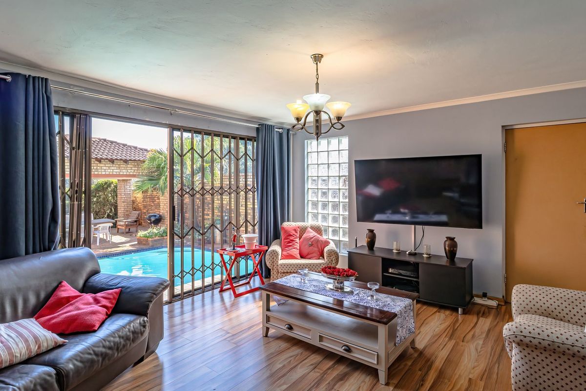 A comfortable living room featuring laminate flooring, a glass block window, and sliding doors that open directly onto the pool area.