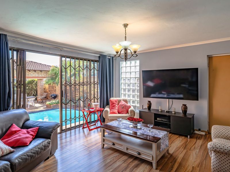 A comfortable living room featuring laminate flooring, a glass block window, and sliding doors that open directly onto the pool area.
