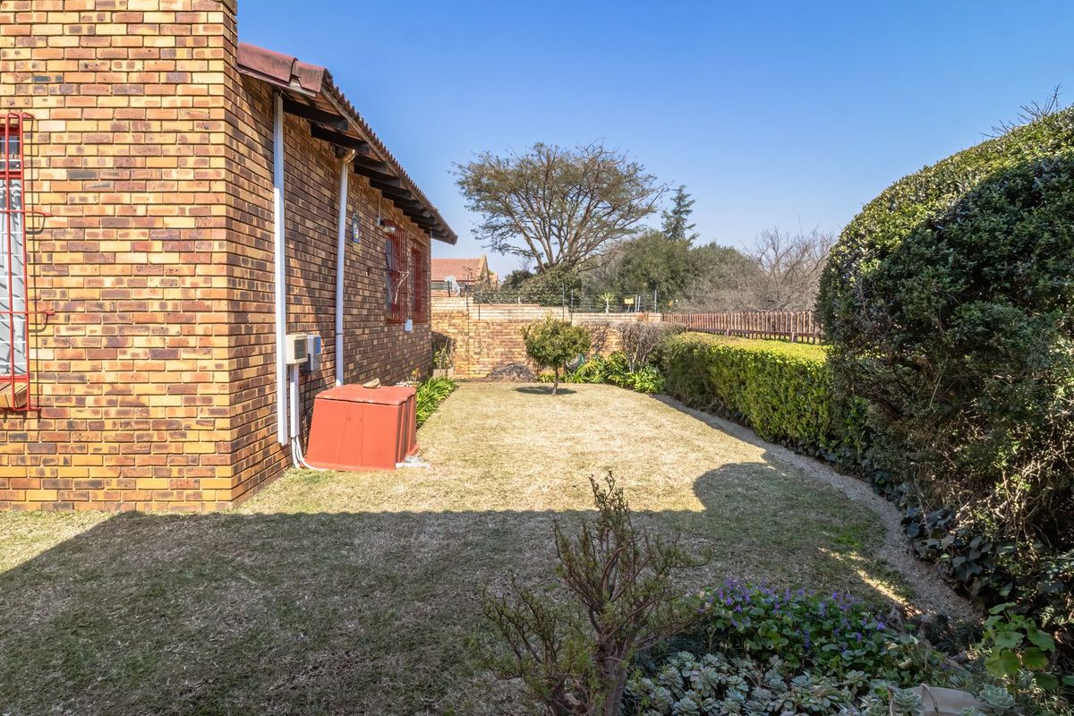A view of the rear garden featuring a face brick exterior wall, established hedging, and a lawn area.