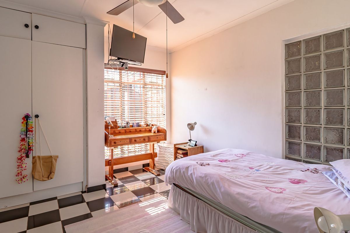 A bedroom featuring built-in cupboards, a unique glass block feature wall, ceiling fan, and checkered tiled flooring.