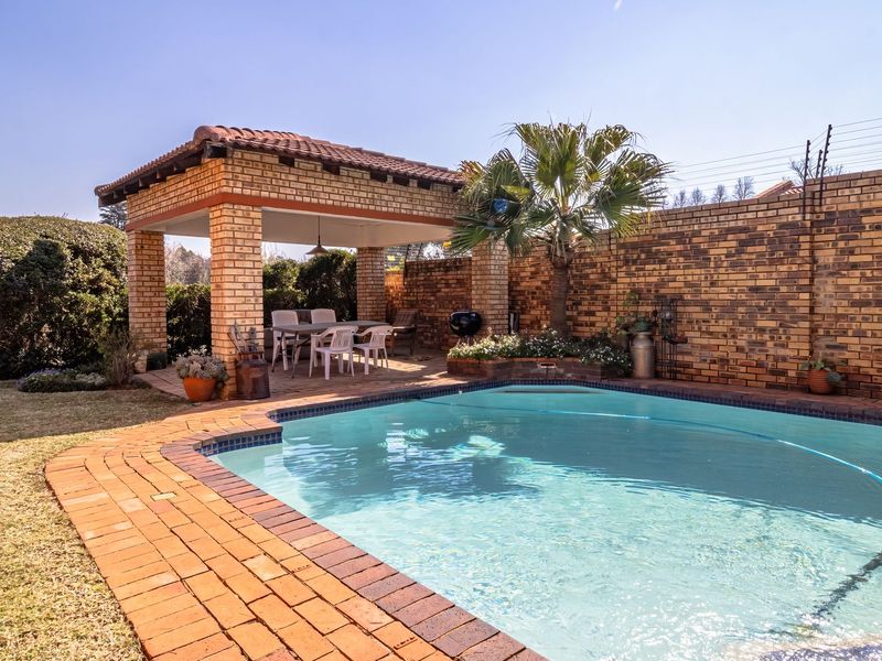 Outdoor entertainment area featuring a swimming pool, brick-paved surround, and a covered patio structure with a tiled roof.