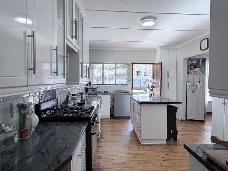 A well-maintained kitchen featuring white cabinetry, dark granite countertops, a gas stove, subway tile backsplash, and a central island with hardwood flooring.