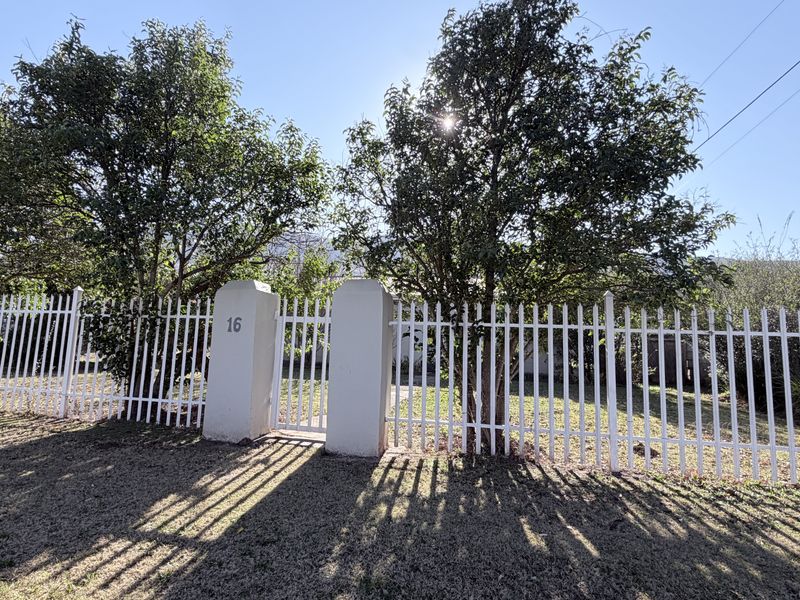 Front view of the property featuring a white metal picket fence and concrete gate pillars with house number 16.