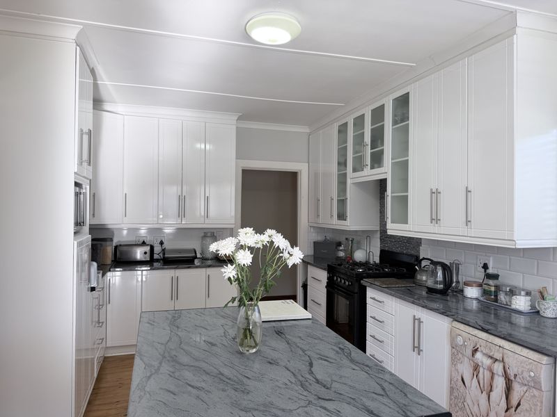 A well-maintained kitchen featuring white shaker-style cabinetry, a stone island countertop, subway tile backsplash, and a black gas stove.