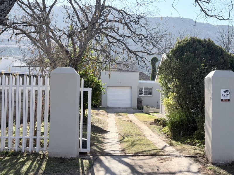 Front view of the property featuring a driveway leading to a garage, secured by a gated entrance with CCTV surveillance.
