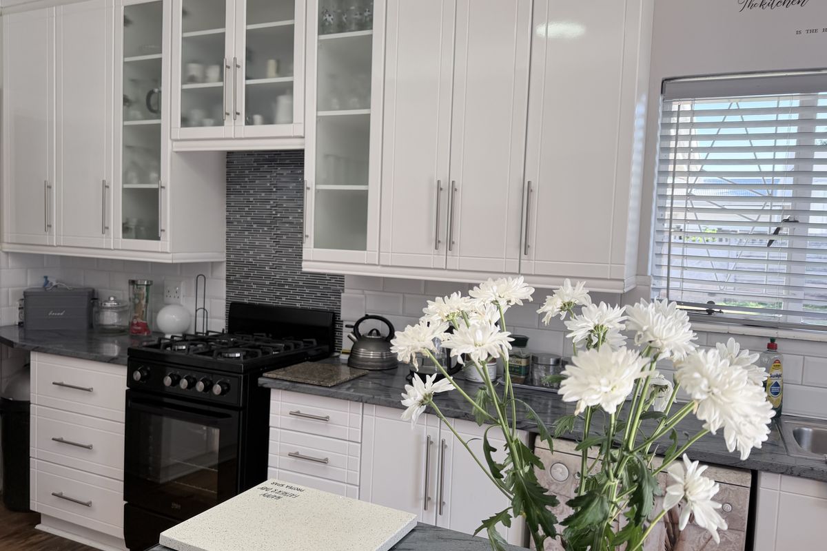 A well-maintained kitchen featuring white shaker-style cabinetry, glass-front display units, a gas stove, and contrasting stone-look countertops with a subway tile backsplash.