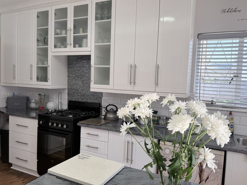 A well-maintained kitchen featuring white shaker-style cabinetry, glass-front display units, a gas stove, and contrasting stone-look countertops with a subway tile backsplash.