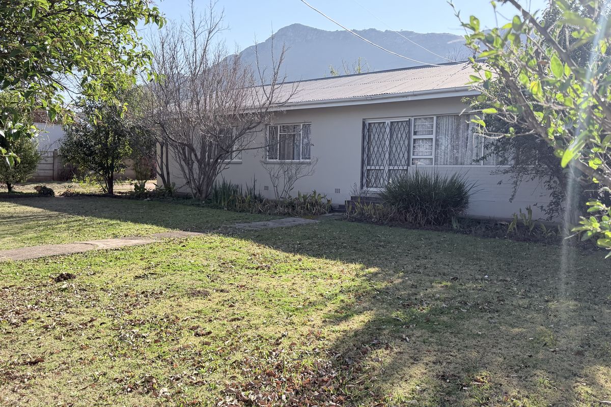 Rear view of a single-story house featuring a metal roof, security gate, and established garden with mountain views.