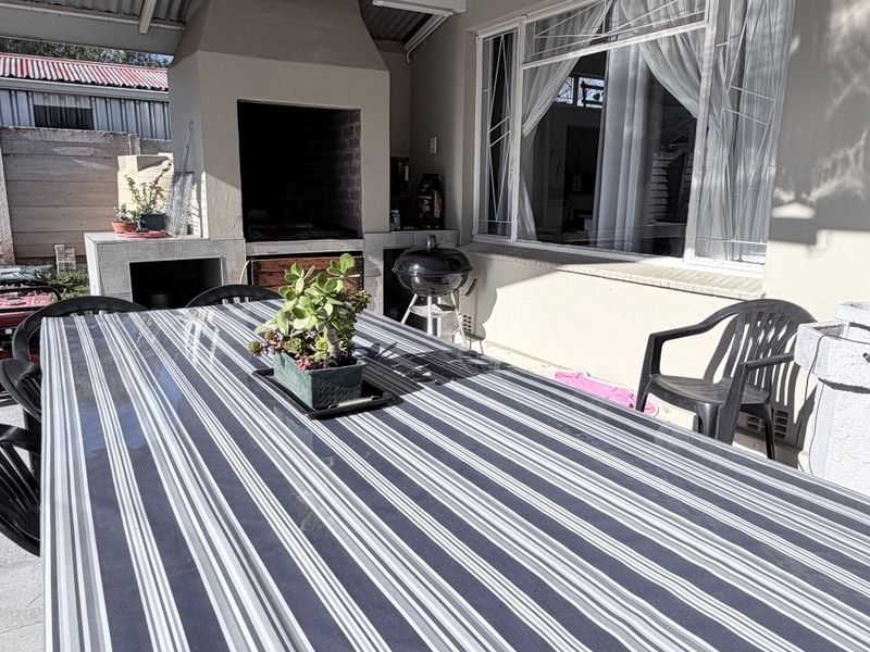 Covered outdoor patio area featuring a built-in braai, tiled flooring, and direct access to the home through a large window.