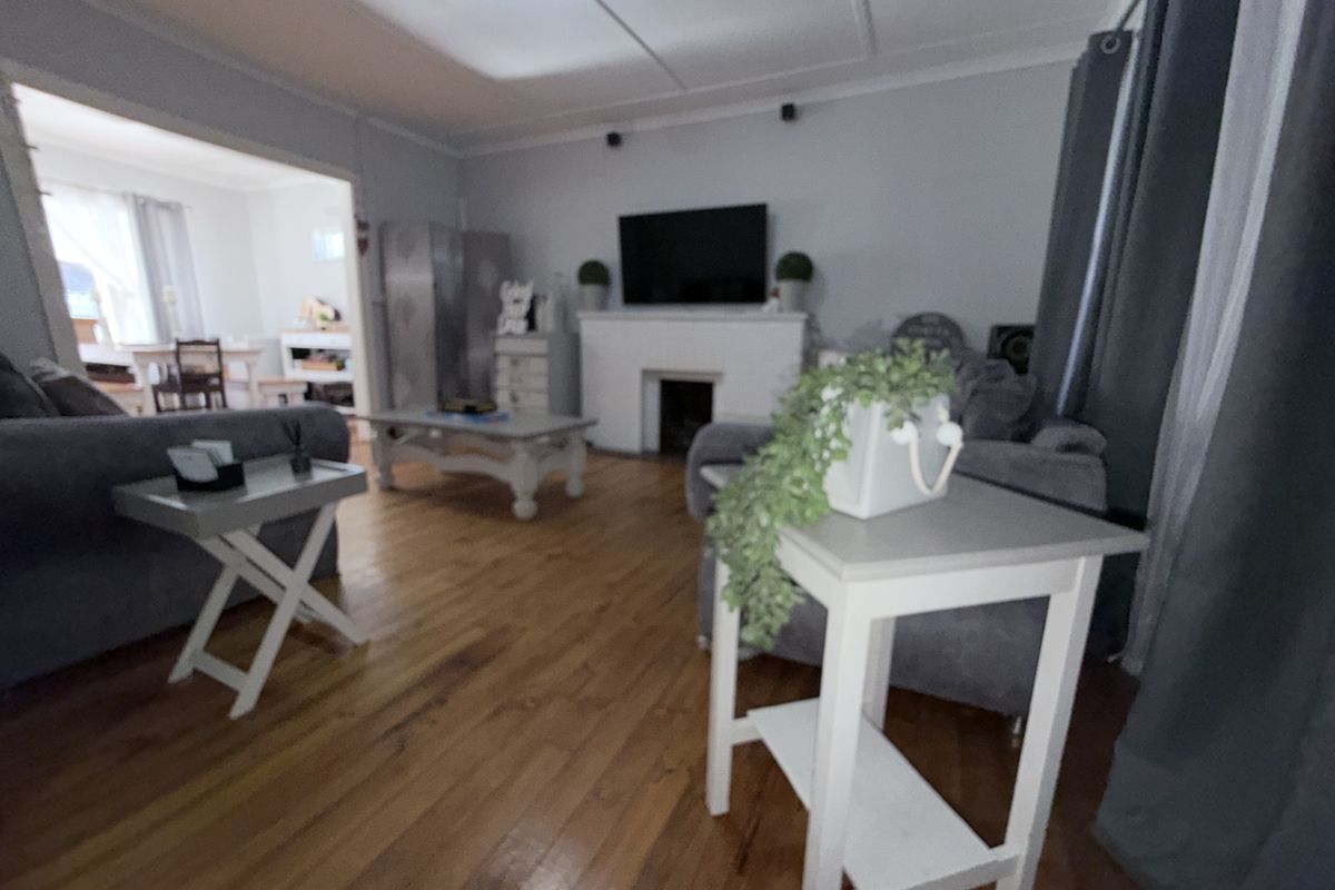 A living room featuring hardwood flooring, a central fireplace, and coved ceilings, with an open-plan flow leading into an adjacent dining area.