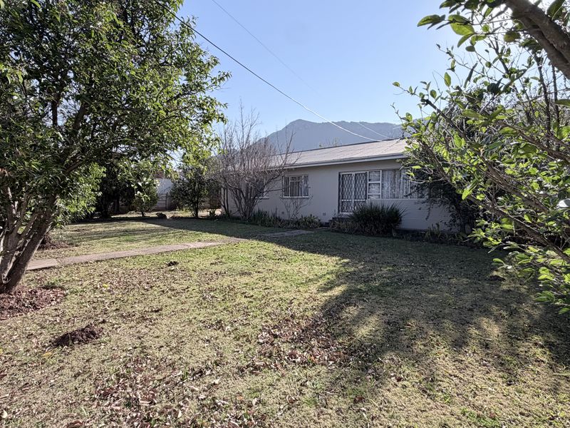 Rear view of the property featuring a spacious garden, paved walkway, and mountain views in the background.