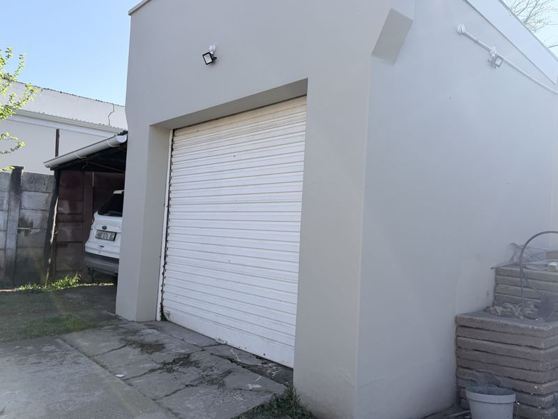 A detached single garage featuring a white roller shutter door, exterior security lighting, and a concrete driveway.
