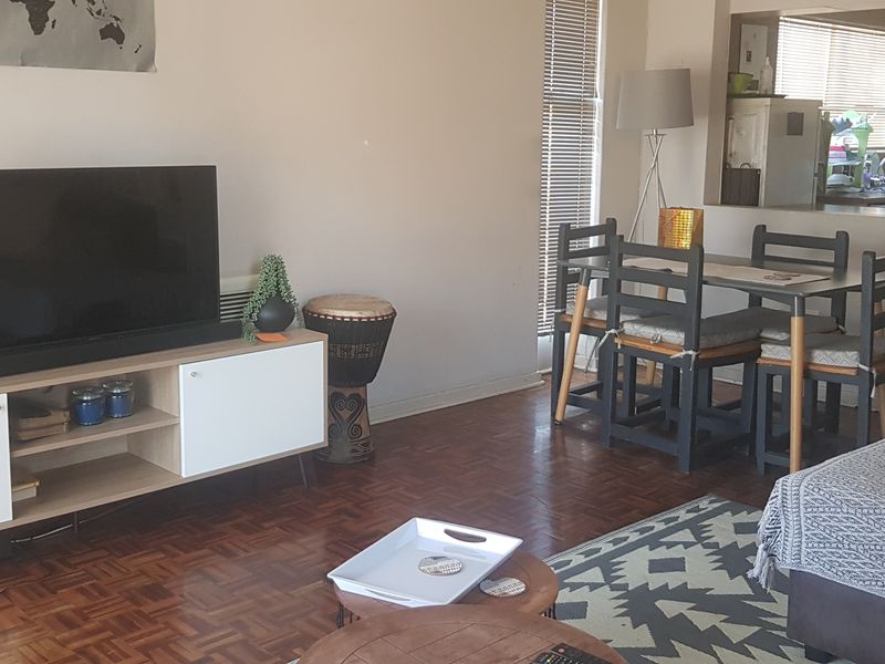 Open-plan living and dining area featuring classic parquet flooring, venetian blinds, and a convenient pass-through window connecting to the kitchen.