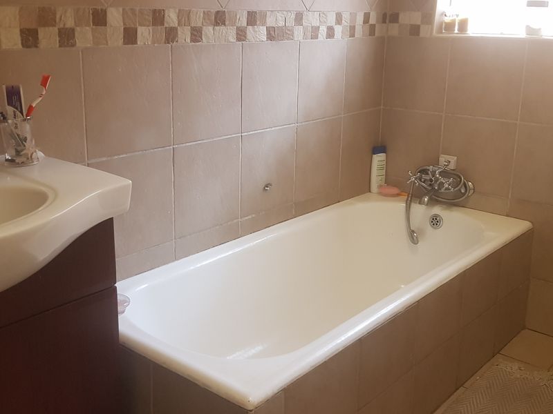 A functional bathroom featuring a built-in bathtub, vanity cabinet with basin, and neutral ceramic wall and floor tiling.
