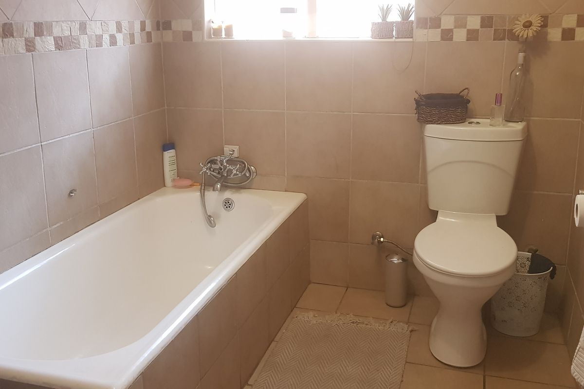 A functional bathroom featuring a bathtub, toilet, and neutral wall and floor tiling with a decorative border.
