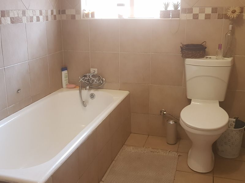 A functional bathroom featuring a bathtub, toilet, and neutral wall and floor tiling with a decorative border.