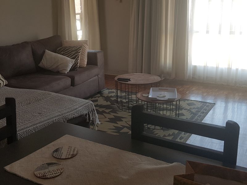 A living room area featuring classic parquet flooring and large windows that provide ample natural light.