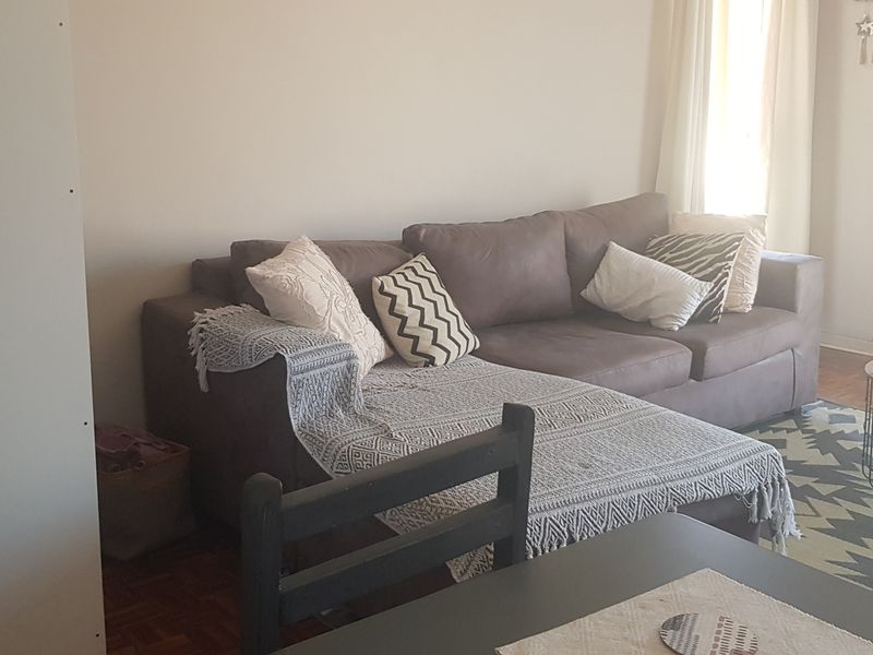 A comfortable living room area featuring classic parquet flooring and natural light from the adjacent window.