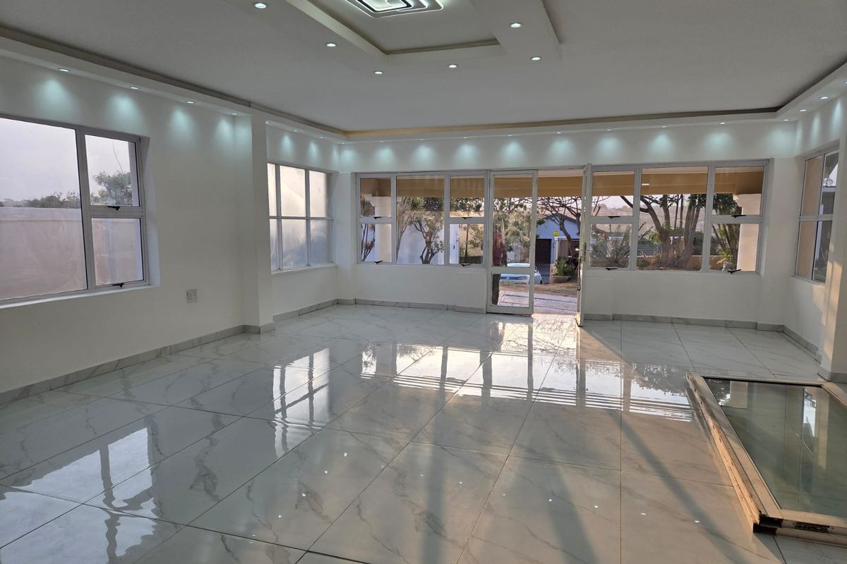 Spacious, light-filled living area featuring modern porcelain floor tiles, a coffered ceiling with recessed lighting, and large aluminium-framed windows and doors.