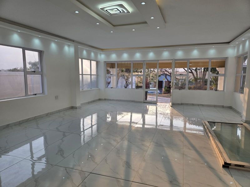 Spacious, light-filled living area featuring modern porcelain floor tiles, a coffered ceiling with recessed lighting, and large aluminium-framed windows and doors.