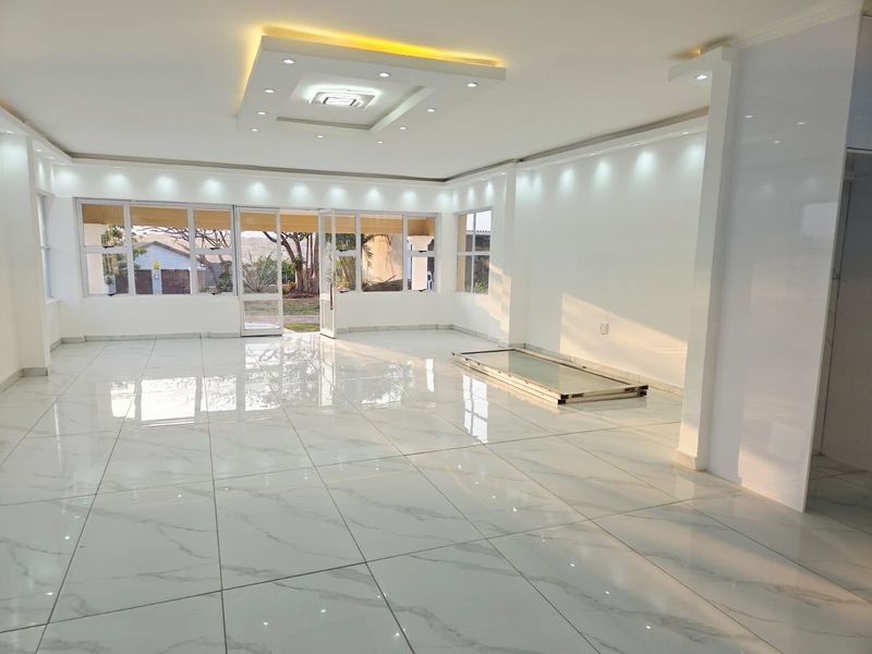 Spacious open-plan living area featuring high-gloss marble-look floor tiles, modern recessed ceiling lighting, and large aluminium-framed windows providing ample natural light.